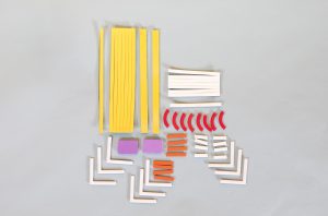 A variety of Picture Maker diagramming strips laid out on a gray background including long yellow strips, white strips in various shapes and lengths, curved red strips, orange strips, and two purple rectangles.