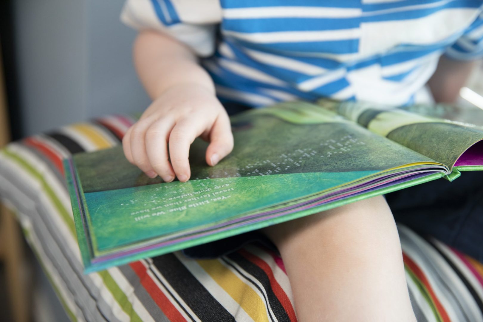 A young child reading the braille on a braille book that is sitting in their lap.