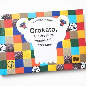 The cover of LDQR's Crokato, the Creature Whose Skin Changes by Claudette Kraemer. The cover has a checkerboard pattern and features the APH and UEB logos.