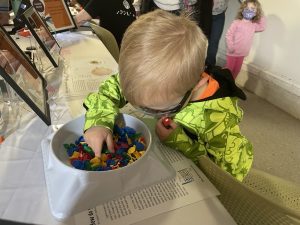 A little boy wearing a neon sweatshirt and glasses searches through a bowl of small plastic toys.