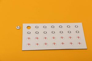 An overhead shot of the red X and black O player token sheet laid on a yellow background.