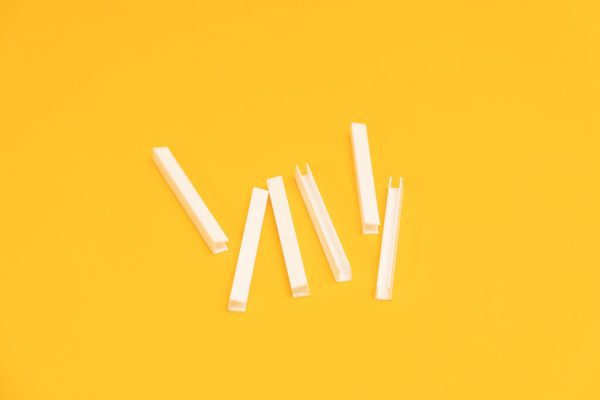 : A close up of six white U-Channels laid out on a yellow background.