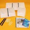 All components of the White Expandable Calendar Boxes kit laid out on a yellow background. Included are six white foam boxes attached to one another with black and white U-channels, two additional large black U-channels, six smaller white U-channels, and the print guidebooks placed in front.