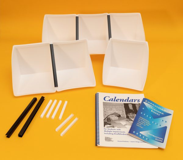 All components of the White Expandable Calendar Boxes kit laid out on a yellow background. Included are six white foam boxes attached to one another with black and white U-channels, two additional large black U-channels, six smaller white U-channels, and the print guidebooks placed in front.