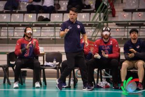 Keith Young coaching at the 2022 IBSA World Goalball Championships. Three players sit on the bench behind him.