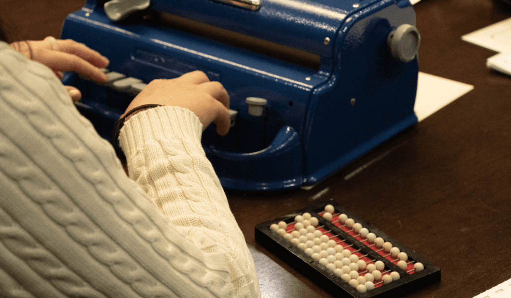 A student types on a Perkins Brailler sitting next to a Cranmer Abacus.