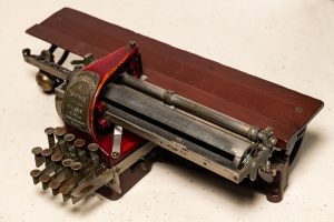 A Kleidograph with metal keys, a reddish wood back, and a metal plate indicating that the braille writer belongs to the