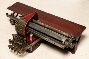 A Kleidograph with metal keys, a reddish wood back, and a metal plate indicating that the braille writer belongs to the 