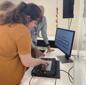 A woman touches the Monarch's braille display as a monitor behind the device displays a graph.