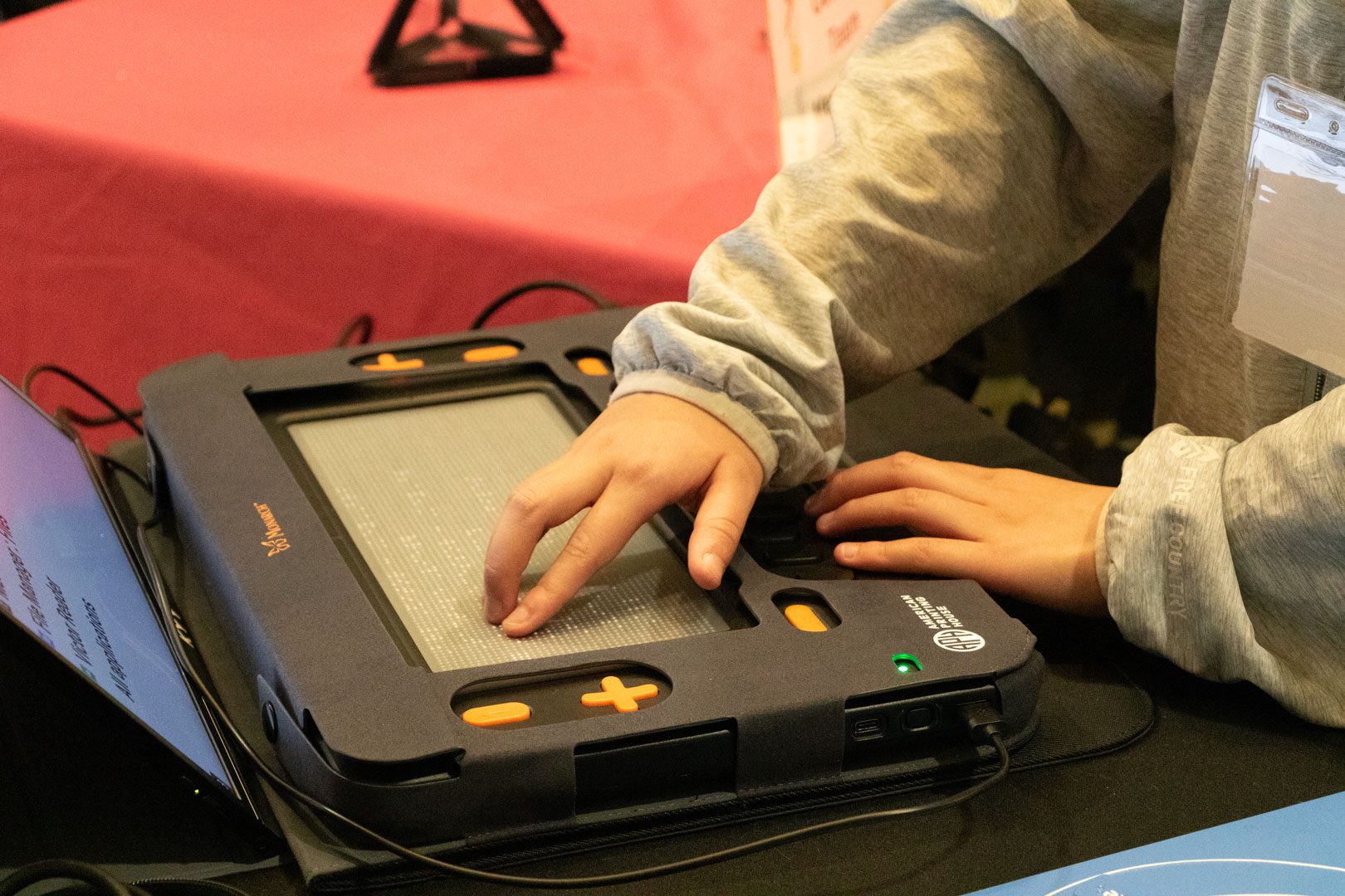 A student uses one hand to touch braille on the Monarch's tactile display. A screen facing the student can be seen behind the Monarch.