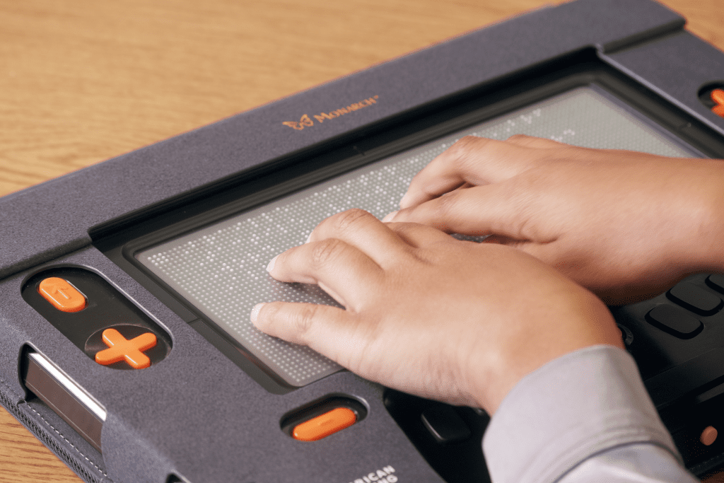 A student using two hands to read braille on the Monarch's refreshable braille display.