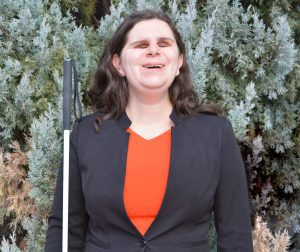 Karen Anderson smiles as she poses for a photo and holds a white cane at her side.