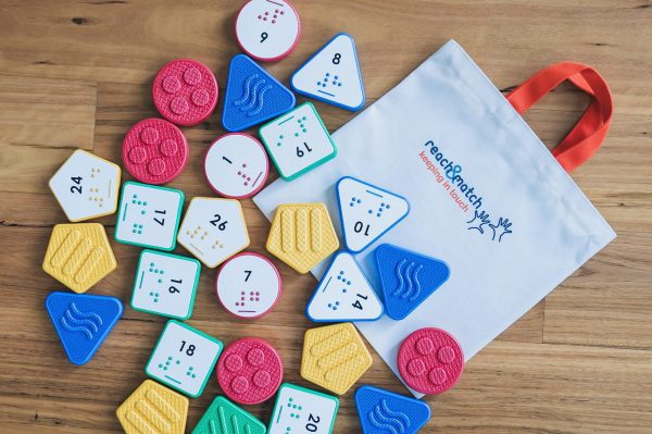 A variety of Reach & Match Number Tiles spread out on a wooden floor on top of a branded "Reach & Match" canvas bag.