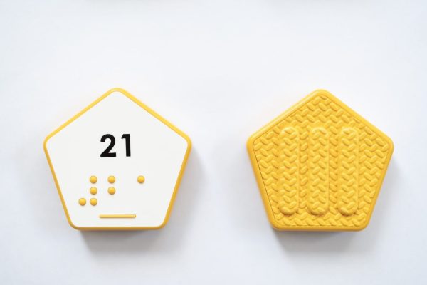 Close up comparison of the front and back of a yellow hexagonal UEB Reach and Match number tile showing the number 21 in braille and print. The back of the piece is textured.