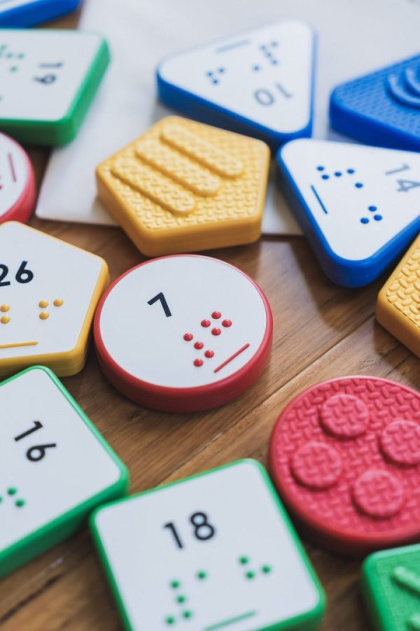 Close up of a variety of multicolored UEB Reach & Match number tiles on a wooden surface