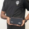 A man wearing a Chameleon cross body and holding the closed device with both hands. The front of the case contains logos for HumanWare and APH.