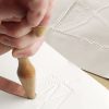 One hand holding the tactile graphics hammer against a point symbol on a white piece of paper.