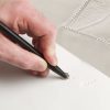 One hand creating a tactile line on a white piece of paper using the tactile graphics kit roller.