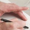 One handing holding a white piece of paper steady while the other hand, holding the tactile graphics kit roller, creates a tactile line.