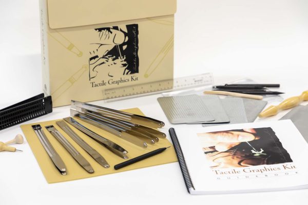 Close up of the tongs and Tactile Graphics Kit print guidebook laid out against a white background. Other kit components lay next to these out of focus.