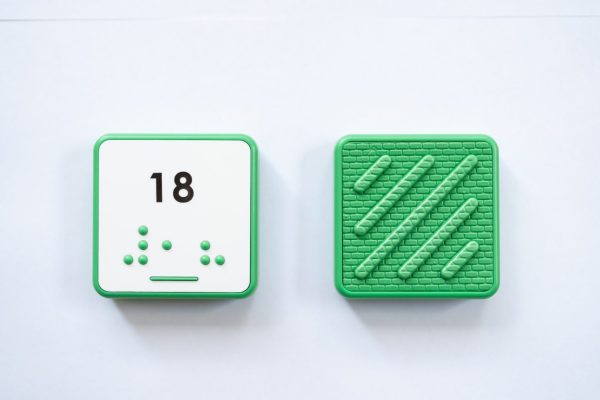 Front and back of green square Reach & Match Number tile showing the number 18 in Nemeth braille and print. The back side is textured.