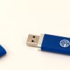 Blue USB thumb drive with the top cover removed. The thumb drive has a white APH logo in its center and sits on a white background.