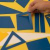 One hand lifts the corner of a nestled rectangle stencil so the outer piece is lifted up.