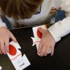 A preschool aged boy in a white shirt with pretzel graphics on it plays with two oval Memory Puzzle pieces.