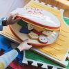 On top of four stacked Reach & Match Light tiles on a wooden floor, two hands open the zip carrying case that contains the Reach & Match Alphabet Tiles.