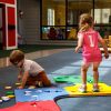 A Reach and Match Light kit assembled on the ground in a path with a little girl jumping along the squares and a little boy playing with tiles on the floor.