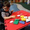 A little boy in a wheelchair with a red Reach and Match foam square on top of his wheelchair tray with a variety of tiles.