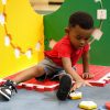 A little boy sitting on the Reach and Match Light kit with the tiles assembled vertically. He is reaching for a yellow tile.