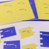 Overhead shot of the Tactile Ionic Bonding Pieces spread out on a white background. Above are four perforated blue and yellow sheets that contain the puzzle pieces, and below are six examples of the puzzle pieces punched out. Nemeth