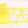 Close up image of the yellow transparent tactile shape slate open to about 45 degrees standing on it's long edge on a white background. On the slate are circles, triangles, squares and more of various sizes.