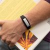A woman's hand holding a closed book with an OpticAware band on her wrist.