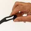A man's hand holding an unfastened black replacement OpticAware band with the center module missing.