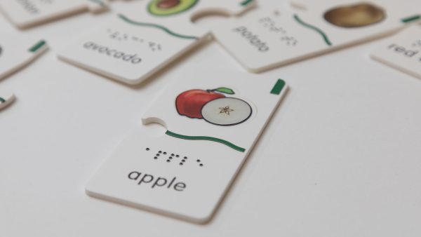 A close-up of the apple puzzle piece that says "apple" in print and braille. The piece has a wavy tactile indicator as well as a small tactile square in the top right corner.