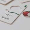 A close-up of the apple puzzle piece that says "apple" in print and braille with the removable apple graphic positioned next to the piece. The piece has a wavy tactile indicator as well as a small tactile square in the top right corner.