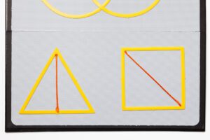 Outlines of a triangle and a square arranged on the blank board of the AnyMath Kit. A median is shown in the triangle, and a diameter is shown in the square.