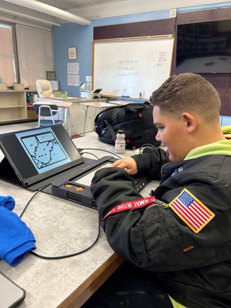 Drew looks at a tactile graphic on the Monarch computer with a smile on his face.