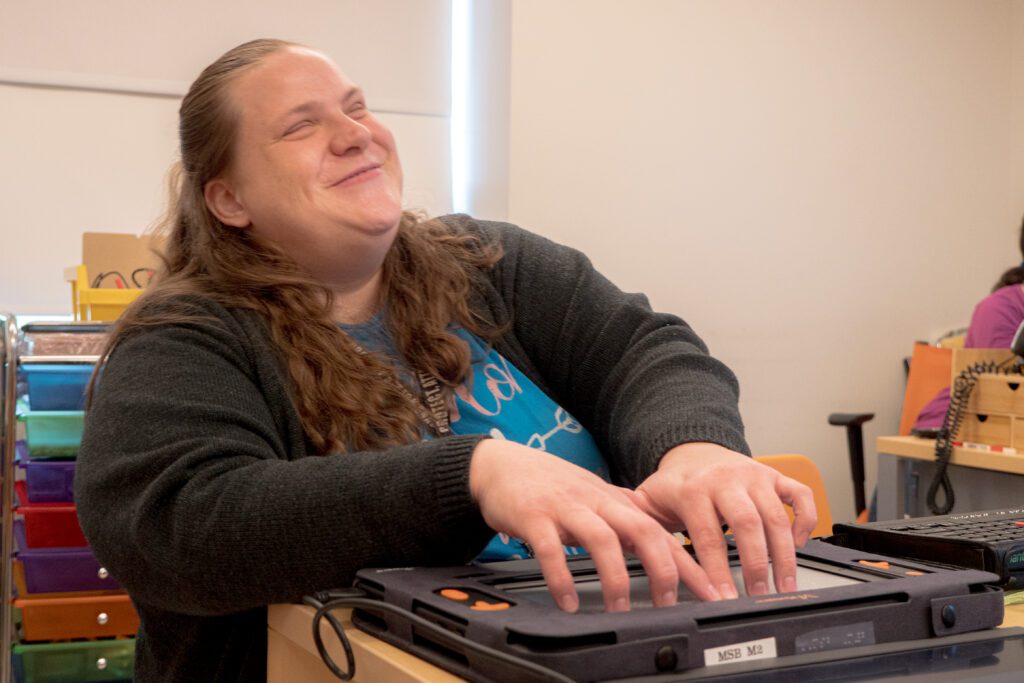A student smiles as her hands explore the braille on Monarch's screen.