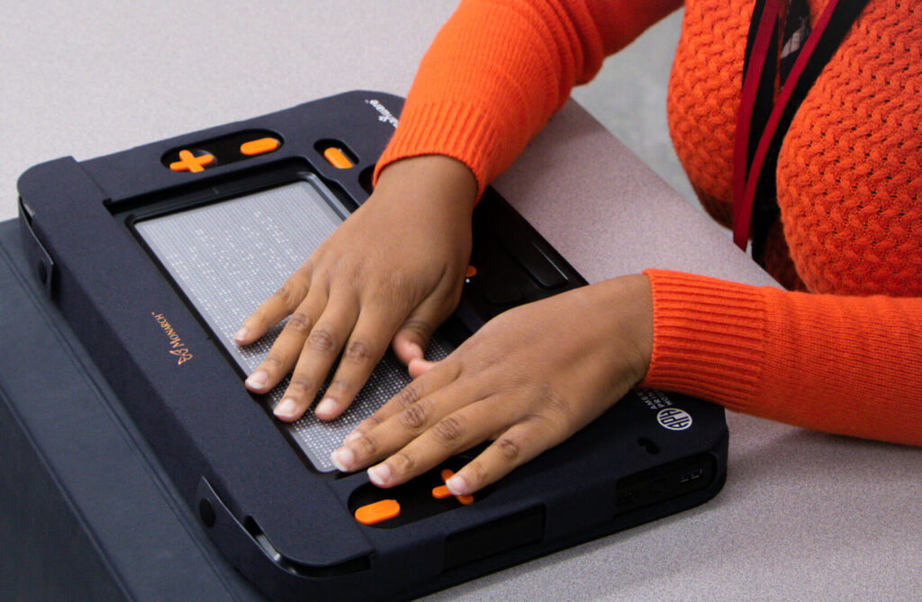 Two hands read braille on Monarch.