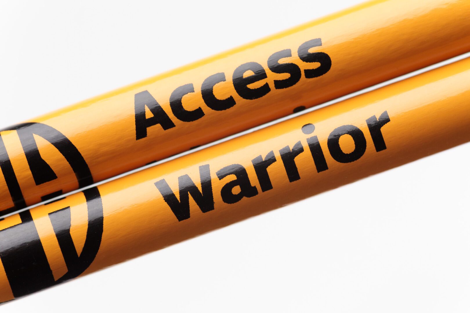 Two gold pencils held closely together to show the full black APH logo. The pencil on top says "Access" and the pencil on bottom says "Warrior."