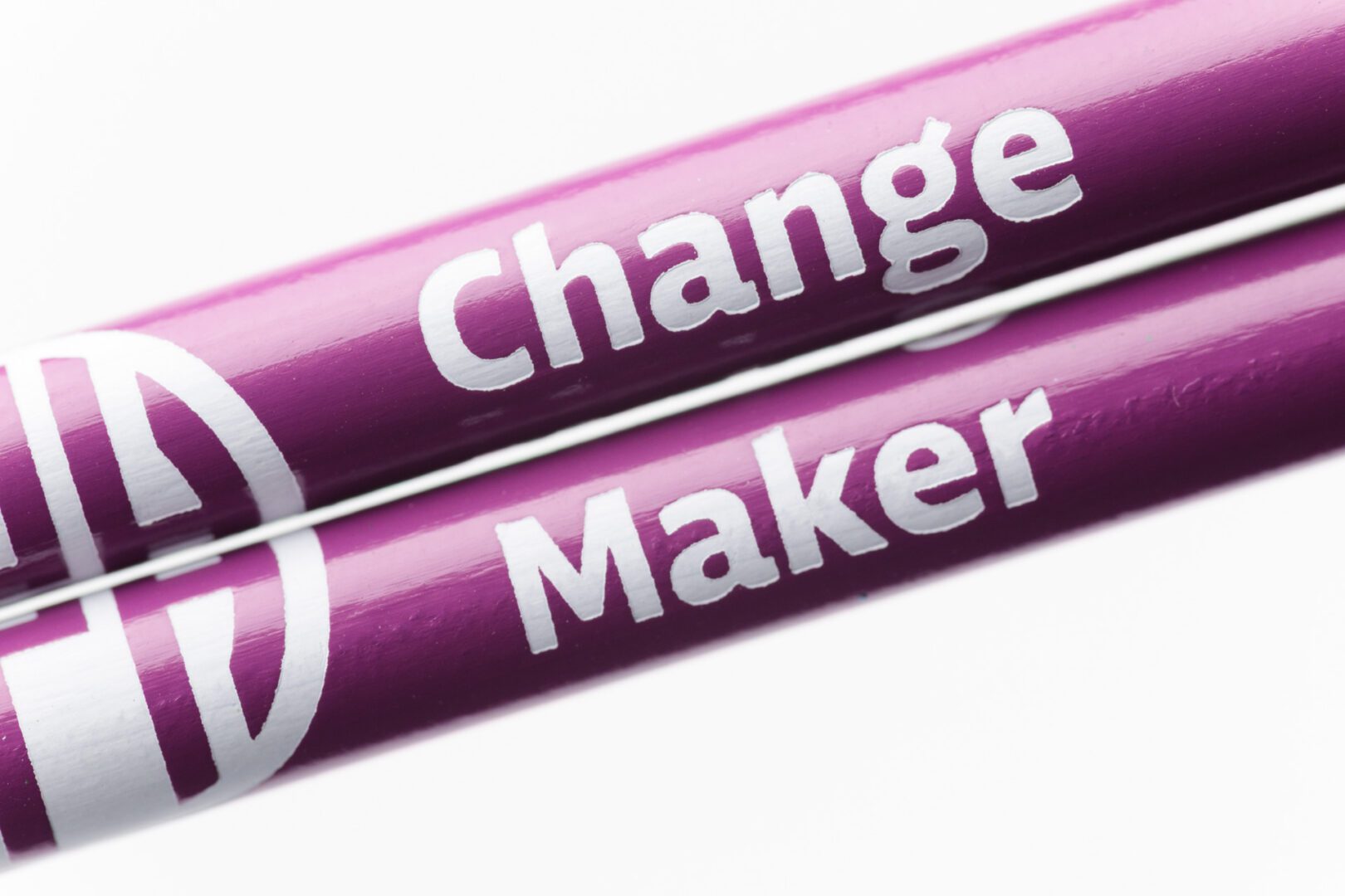 Two purpose pencils held closely together to show the full black APH logo. The pencil on top says "Change" and the pencil on bottom says "Maker."