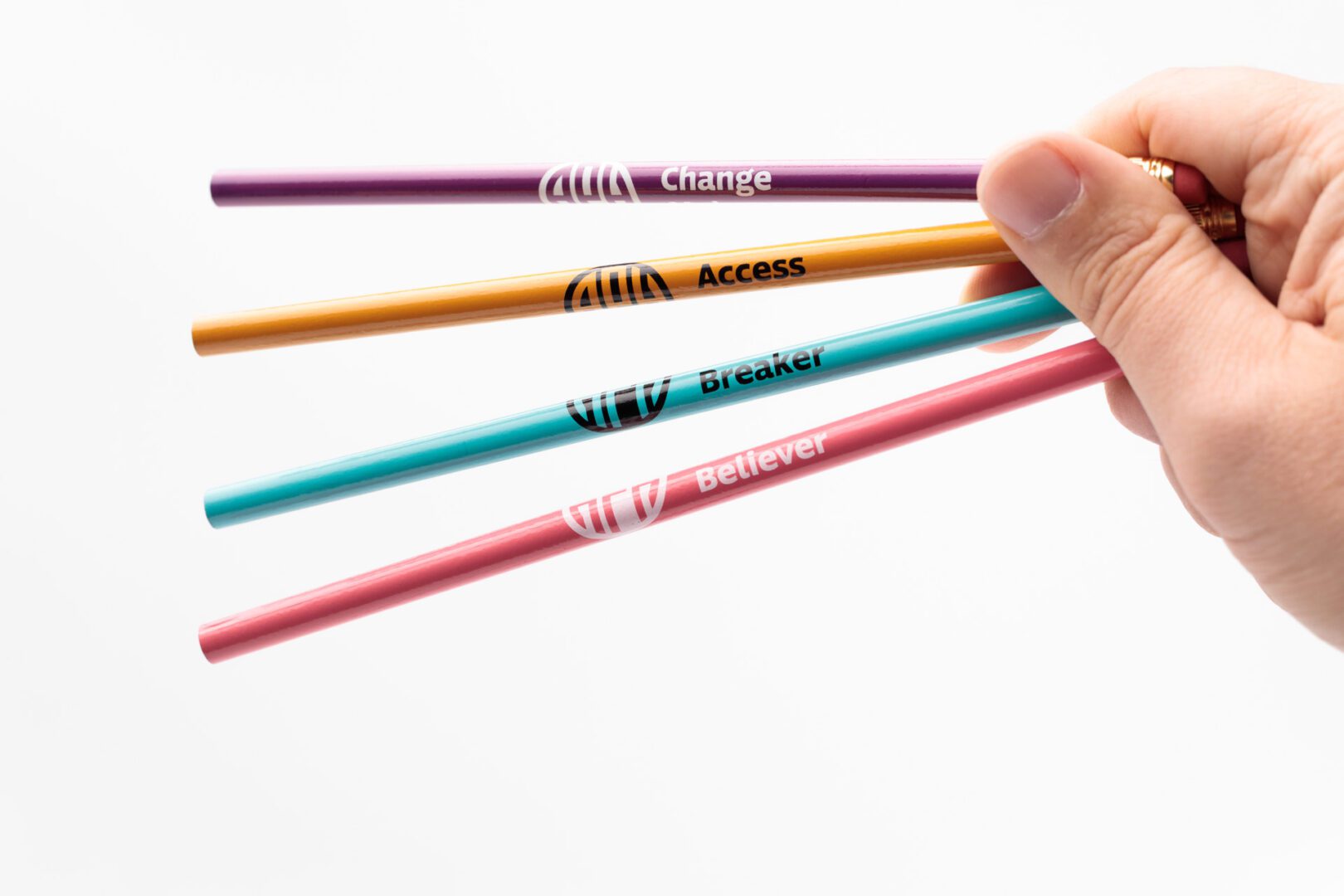 A hand holding one of each color of bold line pencils (gold, teal, pomegranate, and purple).